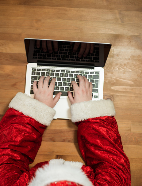 Santa working at desk and typing on a laptop, Christmas gifts an - Фото, зображення