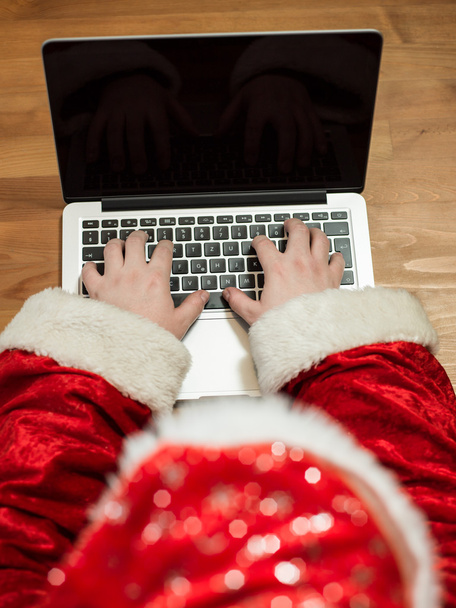 Santa working at desk and typing on a laptop, Christmas gifts and letters, hands top view - Foto, Imagen