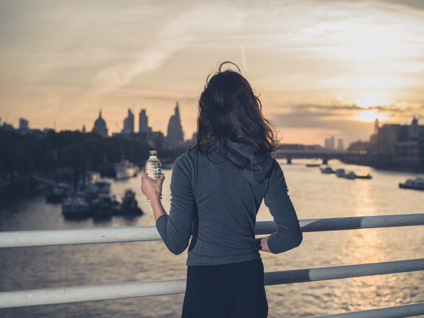 Sporty young woman with bottle on bridge at sunrise - Photo, Image