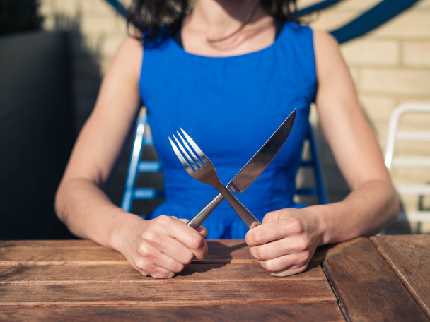 Young woman sitting at table with fork and knife - Foto, afbeelding