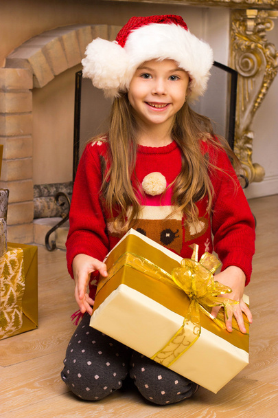 Cute happy girl in red hat holding present near christmas tree - Фото, зображення
