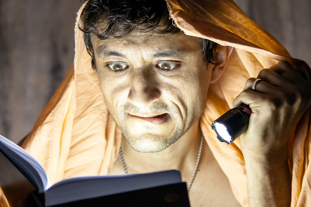 hombre leyendo libro de novela con linterna bajo manta
 - Foto, imagen