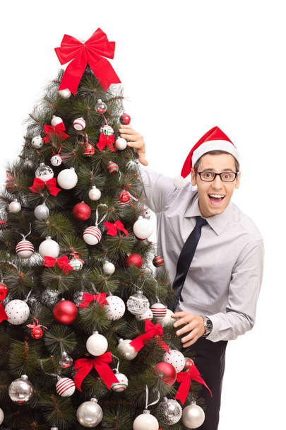 Guy with Santa hat standing by a Christmas tree  - Фото, зображення