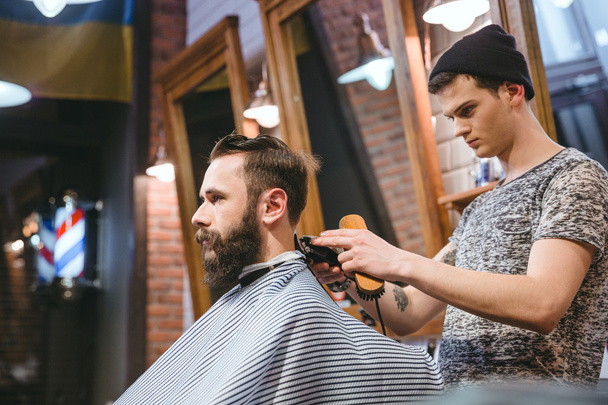 Barber making haircut to handsome man with beard  - Fotó, kép