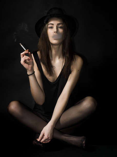 Beautiful girl portrait sitting and wearing hat while smoking ci - Foto, afbeelding