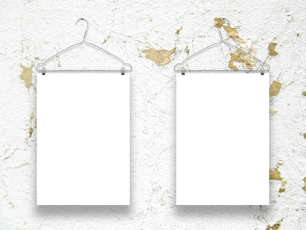 Twee verticale bladen met kleerhangers op verweerde oker- en witte muur - Foto, afbeelding
