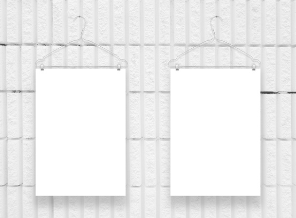 zwei vertikale Blätter im Format A4 mit Kleiderbügeln an weißer Ziegelwand aufgehängt - Foto, Bild