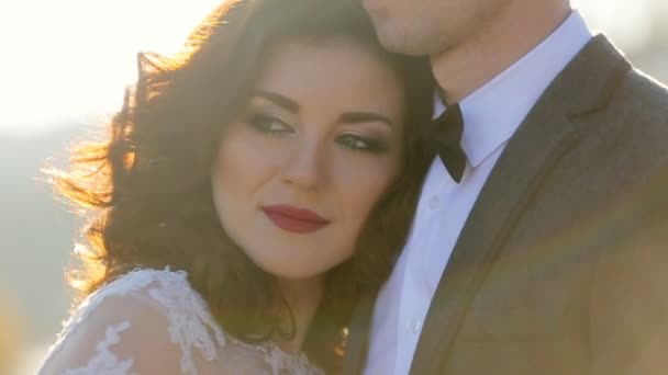 官能的な美しい若いブロンドの花嫁とハンサムな新郎は、スローモーションクローズアップで公園のクローズアップショットで日没で抱き合う - 映像、動画