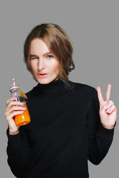 pretty girl in black pullover with bottle of juice in her hand shows v-sign - Foto, Imagen