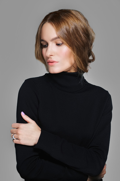 pretty girl in black pullover hugging herself and looking down - Foto, Imagen