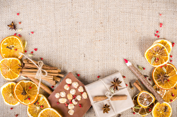 Dried oranges, cinnamon, cloves, cardamom, handmade milk chocolate with nuts, wooden pencil, list of paper on sackcloth, canvas. Christmas, New Year and winter. Free space for your text. - Fotó, kép