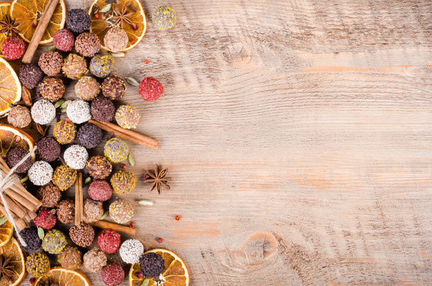 Handmade chocolate candies collection, dried oranges, cinnamon, cloves, cardamom on wooden background. Free space for your text. - Photo, image
