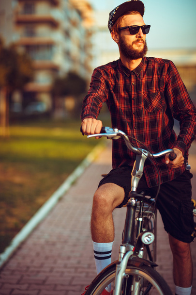 Чоловік в сонцезахисних окулярах їде на велосипеді на міській вулиці
 - Фото, зображення