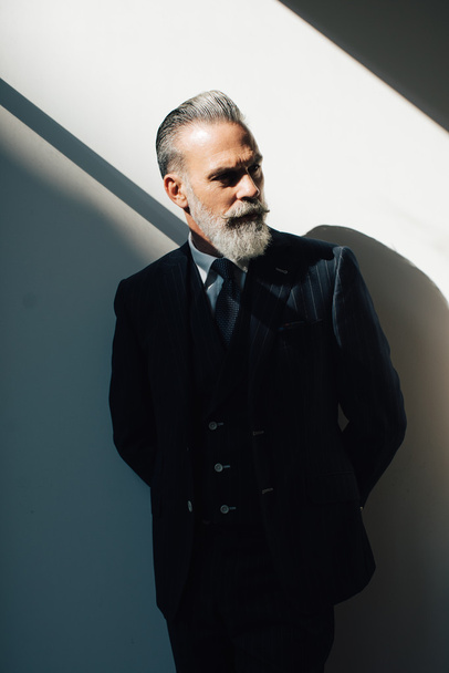 Portrait of bearded man wearing trendy suit and stands against the wall - 写真・画像