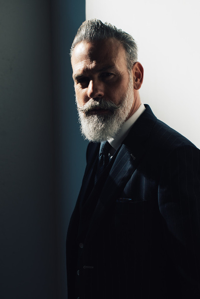 Portrait of bearded man wearing trendy suit and stands against the wall - Photo, image