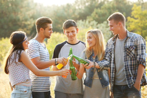 Smiling friends relaxing and clinking bottles in the forest outdoors - 写真・画像