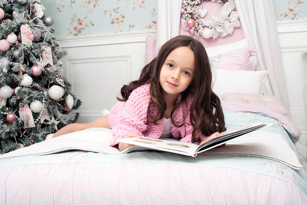 The little girl on her bed reading a book next to tree - Foto, Imagen