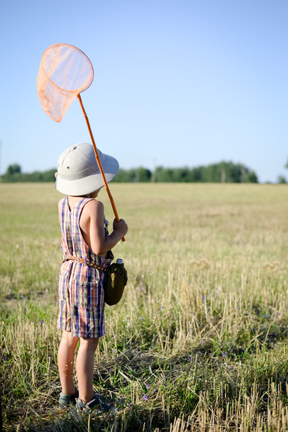 Back view of little boy with butterfly net standing on background field - Photo, Image