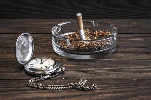 Orologio da tasca vintage e sigaretta spiegazzata in portacenere di vetro sul vecchio tavolo di legno
 - Foto, immagini