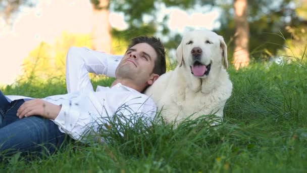 Junger Mann liegt mit Labrador-Hund auf der Wiese - Filmmaterial, Video
