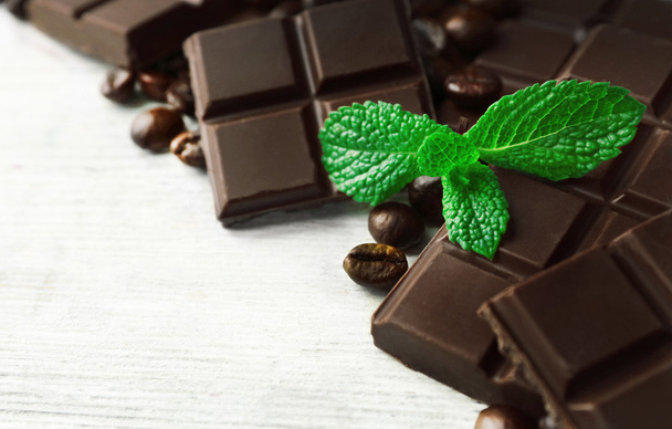 Black chocolate pieces and mint leaves on color wooden background - Photo, Image