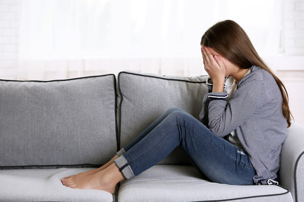 Joven chica molesta llorando en el sofá en su habitación
 - Foto, imagen