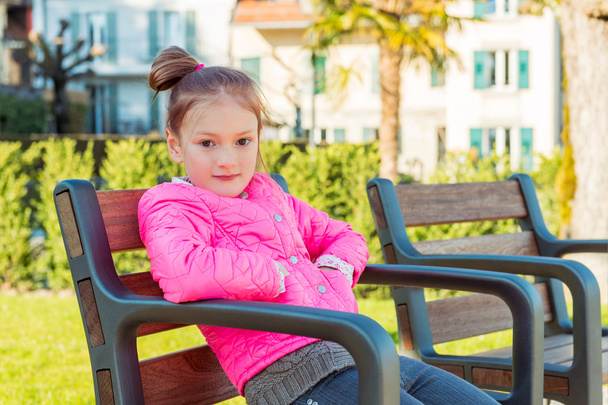 Little girl resting in the park on a nice sunny spring day, wearing bright pink jacket - Φωτογραφία, εικόνα