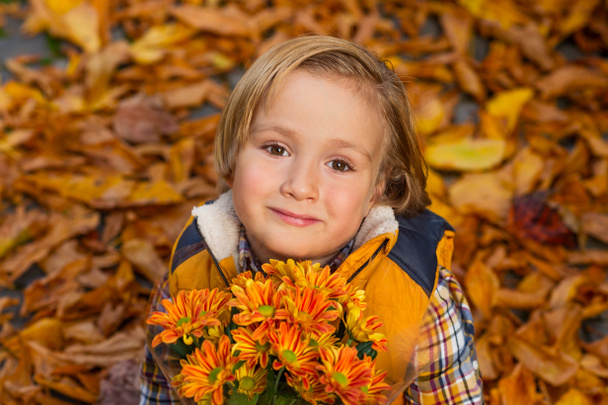 Portrait d'automne d'un adorable petit garçon blond de 4 ans, vêtu d'un gilet jaune chaud, tenant un petit bouquet de fleurs de chrysanthème orange
 - Photo, image