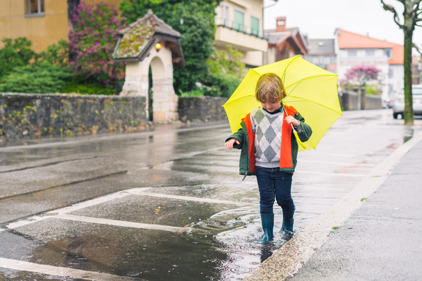 Outdoor Portret van schattige kleine blonde jongen met paraplu onder de regen, spelen in de plas - Foto, afbeelding