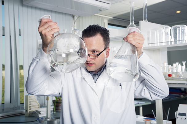 Asistente de laboratorio mirando en una botella con líquido
 - Foto, Imagen