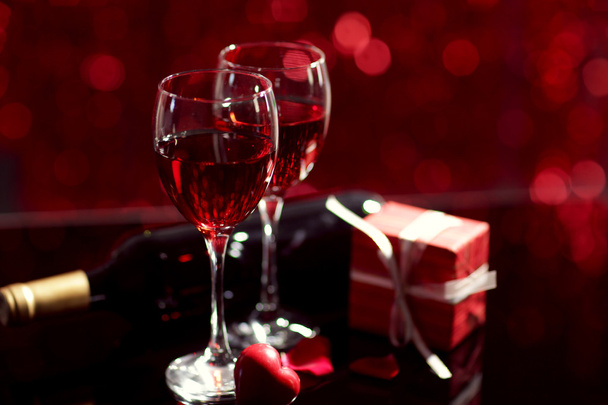 Setting of glasses with wine, bottle and a gift in the box, on red blurred background - Foto, afbeelding