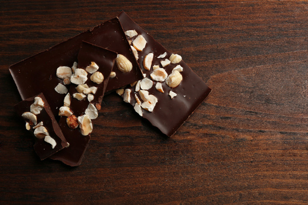 Chocolate pieces with nuts on color wooden background - Foto, Imagem