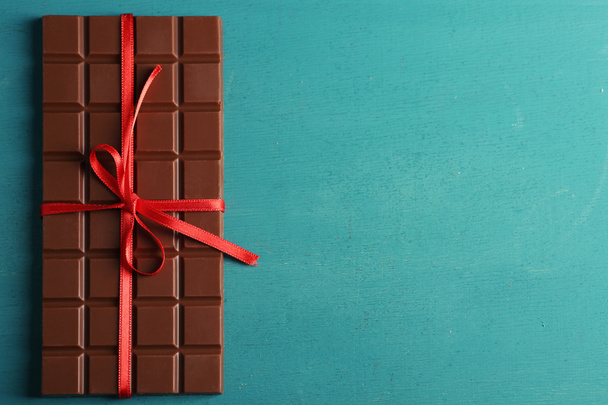 Milk chocolate bar with red bow on color wooden background - 写真・画像
