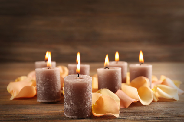 Alight wax grey candle with flower petals on wooden background - Foto, immagini