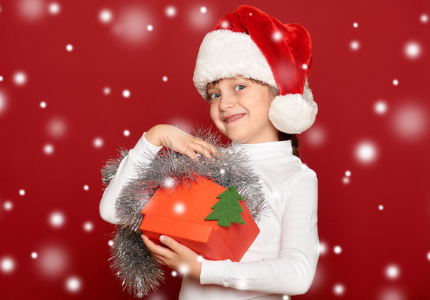 happy girl in hat with box gift show fir tree wool toy on red background - Fotoğraf, Görsel