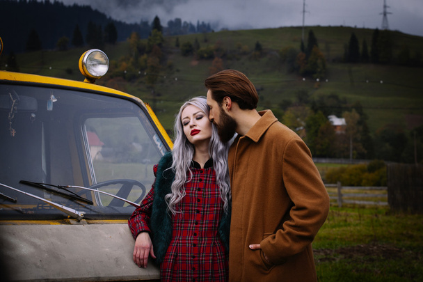 Pareja enamorada cerca de coche amarillo en las montañas Karpathian
 - Foto, imagen