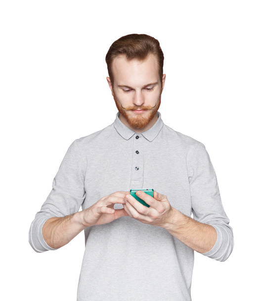 Young man with beard and a mustache standing on white isolated background and holding mobile phone - Φωτογραφία, εικόνα