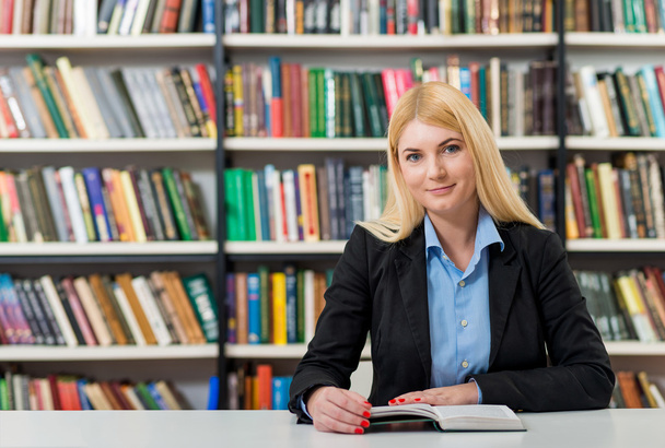 lächelndes junges Mädchen mit blonden Haaren sitzt an einem Schreibtisch im - Foto, Bild