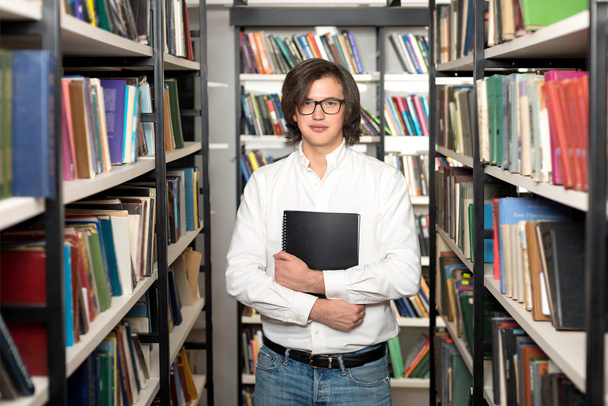 mladý muž s tmavými vlasy, stojí a drží knihu černé kopie  - Fotografie, Obrázek