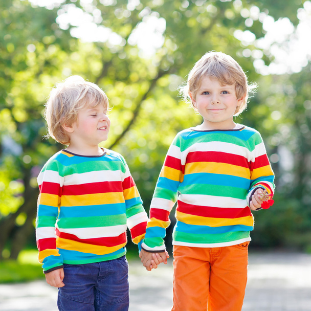 Δύο αδέλφια μικρό παιδιά σε πολύχρωμα ρούχα περπάτημα χέρι μου - Φωτογραφία, εικόνα