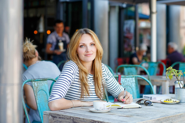 Kobieta pije kawę i pisanie notatek w kawiarni - Zdjęcie, obraz