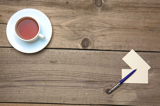 Пустые визитки с ручкой и чайной чашкой на деревянном столе офиса
 - Фото, изображение