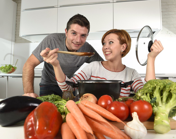 joven atractiva pareja en casa cocina con hombre degustación vegetal guiso cocinado por su esposa sonriendo feliz
 - Foto, imagen