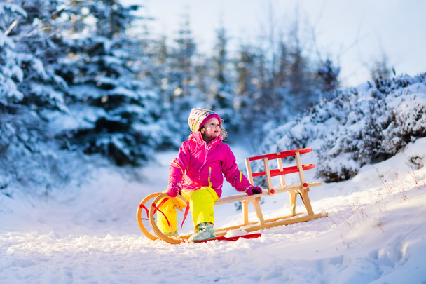 Little girl having fun on a sledge in snowy winter forest - Photo, Image