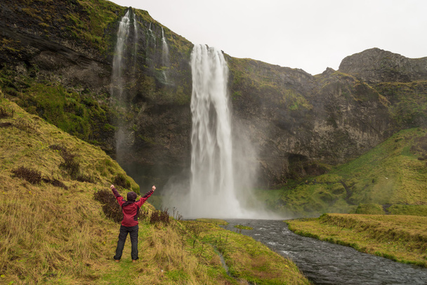 Счастливая женщина у водопада Скогафосс на Исландии позирует безмятежной
 - Фото, изображение