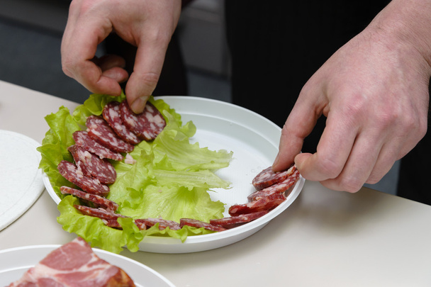 Man sliced sausage on white plate with leaf of salad - Photo, Image