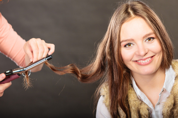 Stylist curling hair for young woman. - Photo, Image