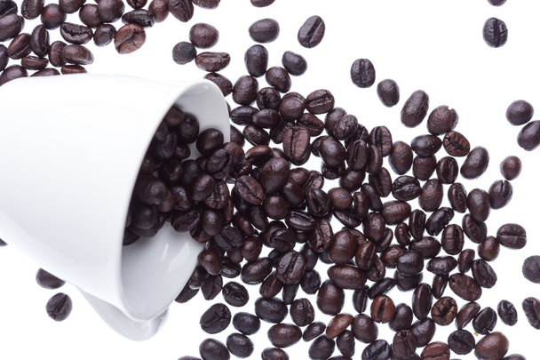 Пролитые кофейные зерна из белой керамической чашки
 - Фото, изображение