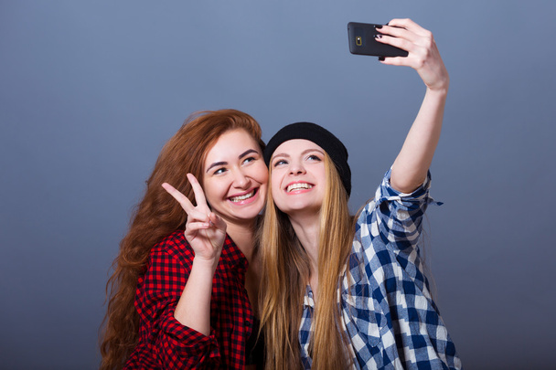 Две молодые улыбающиеся женщины делают селфи с помощью мобильного телефона
 - Фото, изображение