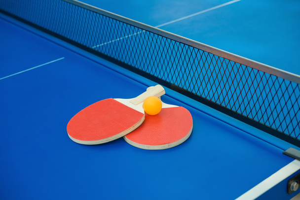 raquetes de pingpong e bola e rede em uma mesa de pingpong azul
 - Foto, Imagem